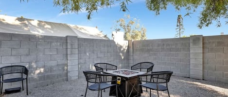 An outdoor patio with a table and chairs, surrounded by a concrete wall and gravel ground.