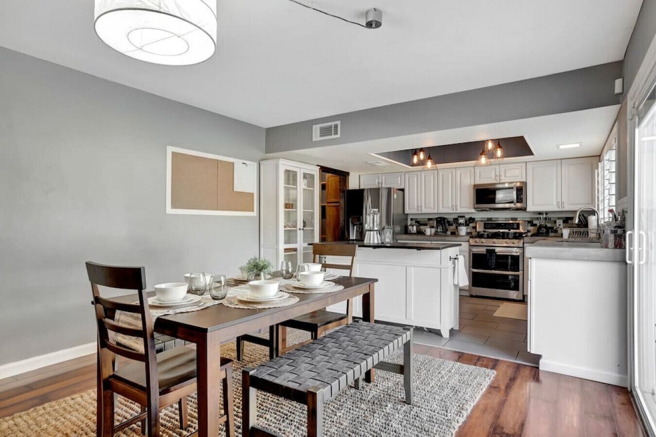 A modern kitchen with white cabinets, a central island, and a dining area with a wooden table and chairs.