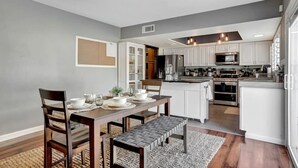 Une cuisine moderne avec des meubles blancs, un îlot central et un coin repas comprenant une table et des chaises en bois.