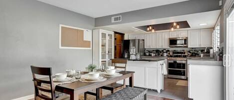 A modern kitchen with white cabinets, a central island, and a dining area with a wooden table and chairs.
