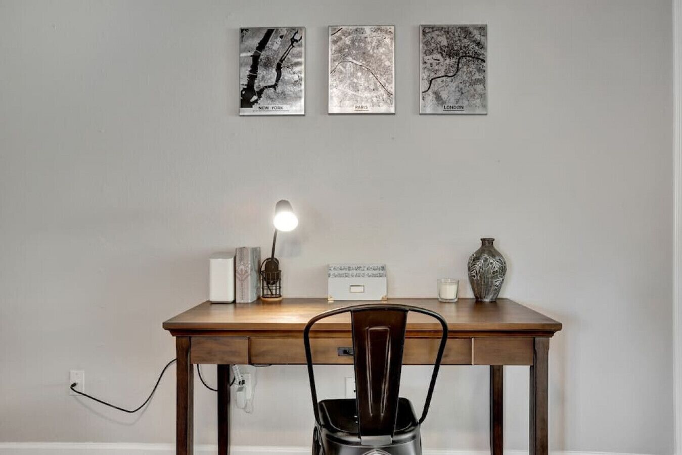 Un bureau en bois, une lampe, un vase et des photos encadrées représentant des paysages urbains.