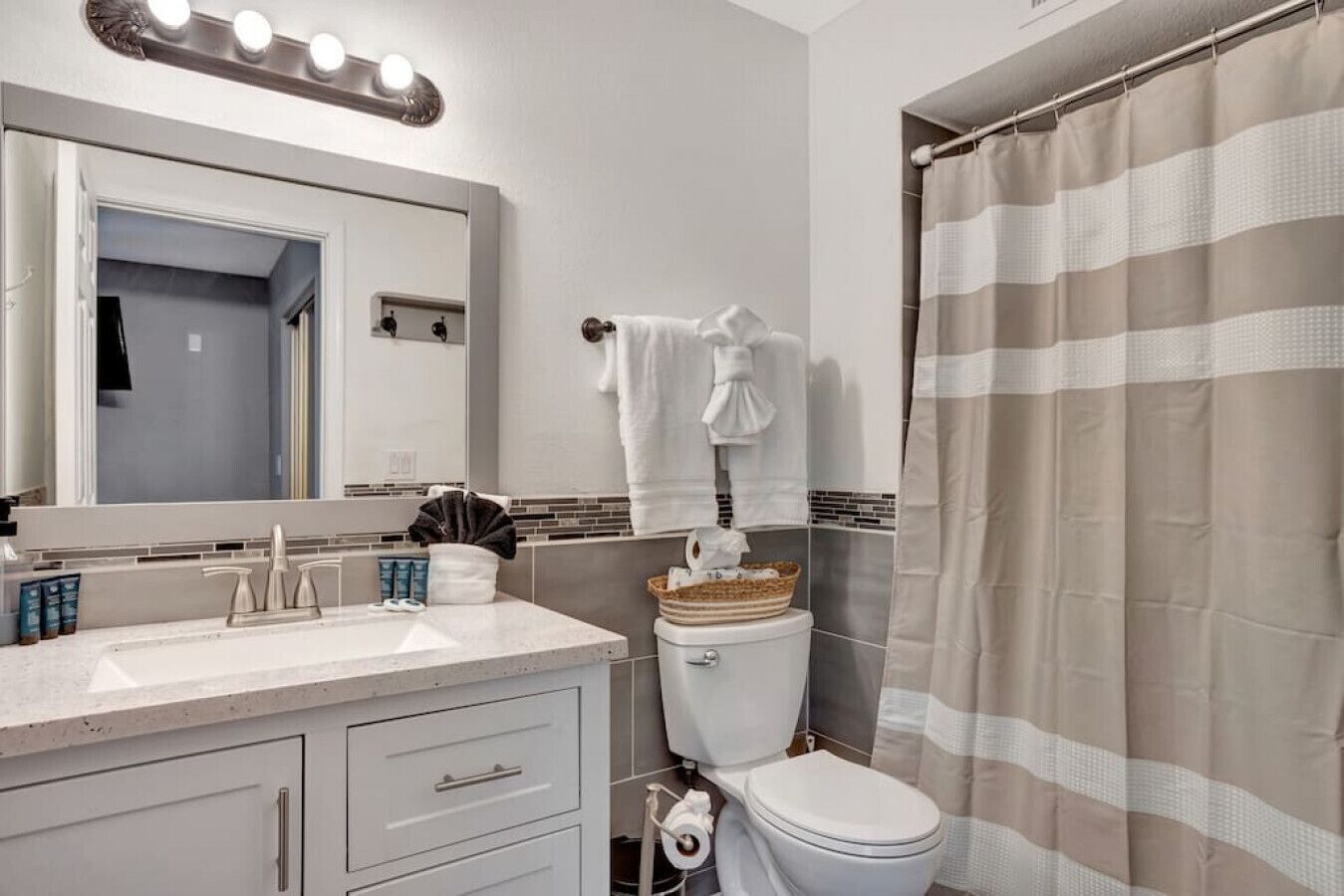 A bathroom with a vanity, a toilet, a shower curtain, and a mirror with lights.