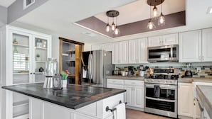 Une cuisine moderne avec des meubles blancs, un îlot central, des appareils en acier inoxydable et des luminaires suspendus.