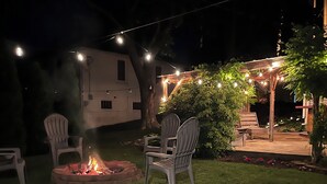 Un espace extérieur aménagé pour les soirées, avec un foyer, des guirlandes lumineuses et des chaises.
