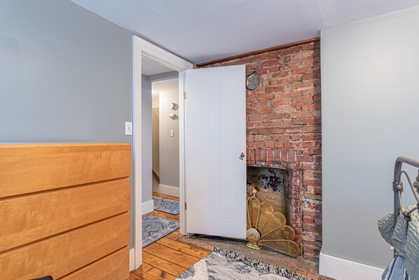 A room with a wooden floor, a white door, a brick fireplace, and a blue rug. - Adorable Kingston Cottage in the Heart of the Roundout Historic Area Downtown. (Kingston)