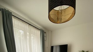Una sala de estar moderna con piso de madera, un sofá gris, una mesa de centro redonda con un control remoto, un televisor en la pared y una planta en maceta.