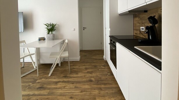 Una cocina moderna con armarios blancos, encimera negra y suelo de madera.