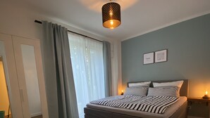Un dormitorio con cama, armario, ventana con cortinas e iluminación en el techo.