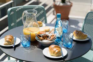 Ein runder Tisch mit einer Karaffe, Croissants, einer Schale Austern sowie Gläsern mit Orangensaft und Wasser.