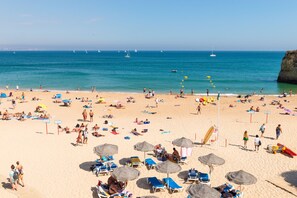 Ein Strand mit Liegestühlen und Sonnenschirmen, ein klarer Himmel sowie Segelboote in der Ferne.
