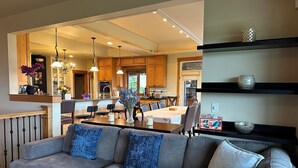A modern living room with a grey sofa, dining area, kitchen, and built-in shelves.