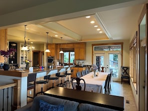 A spacious kitchen with wooden cabinets, a central island, bar stools, and pendant lighting.