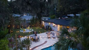 Un patio trasero con piscina, mobiliario exterior e iluminación colgante.