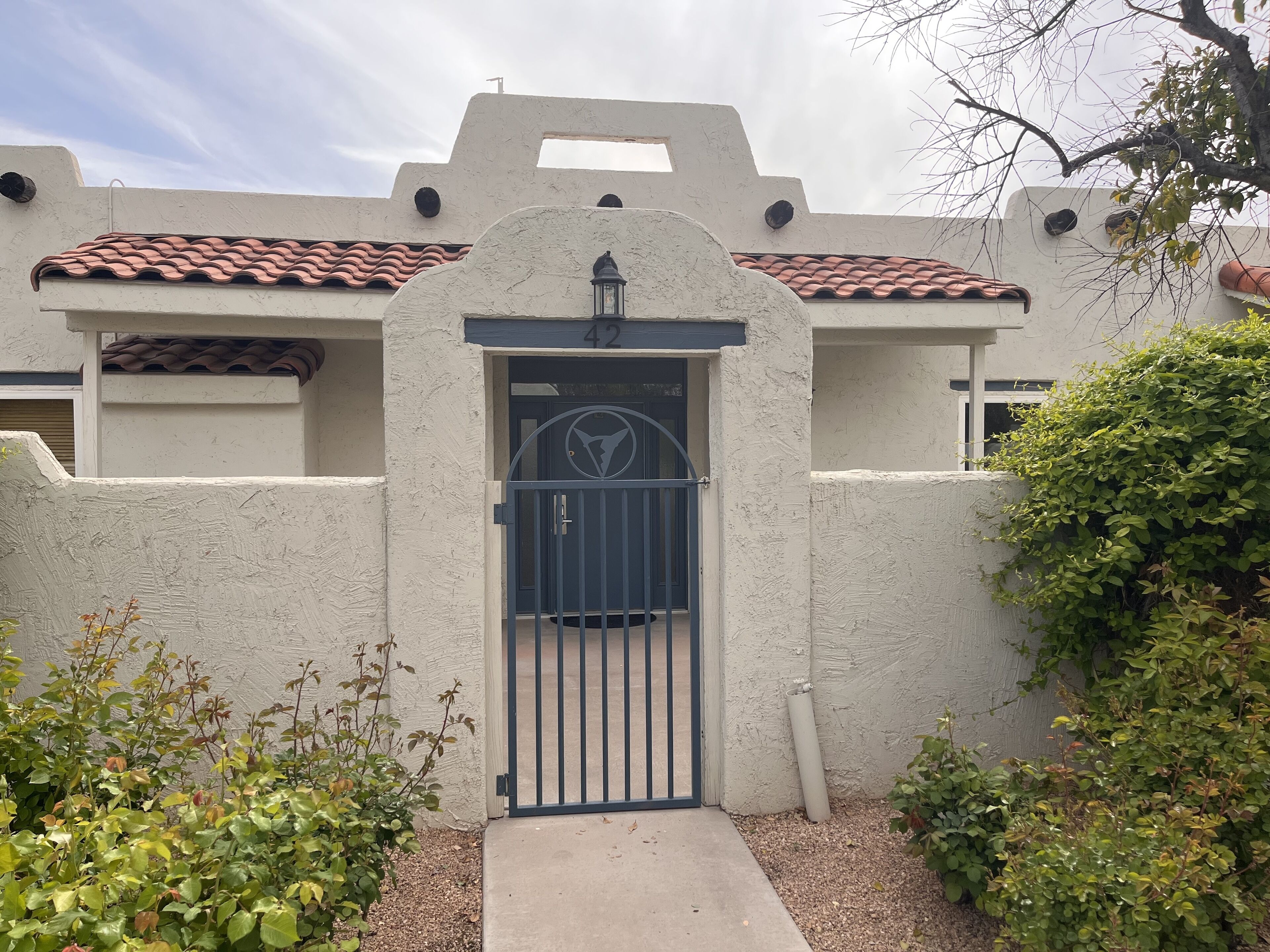 A building with a white stucco exterior, a red-tiled roof, and a black metal gate.