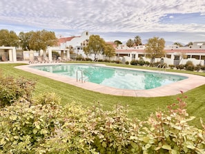 A swimming pool surrounded by a well-maintained lawn and a row of white buildings with red-tiled roofs. - 42-Resort Condo, Pool, Hot Tub, Pickle-ball, Gym. (St. George)