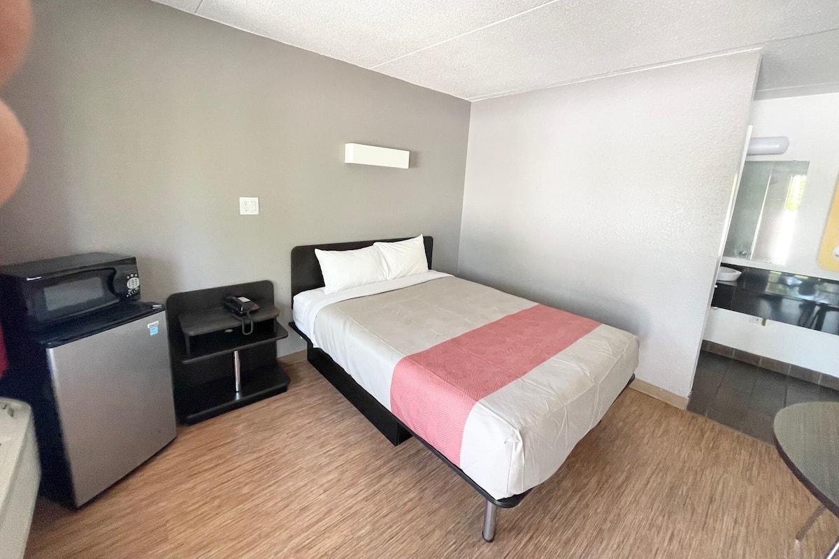 Una habitación de hotel con una cama, un escritorio con microondas y una pequeña kitchenette.