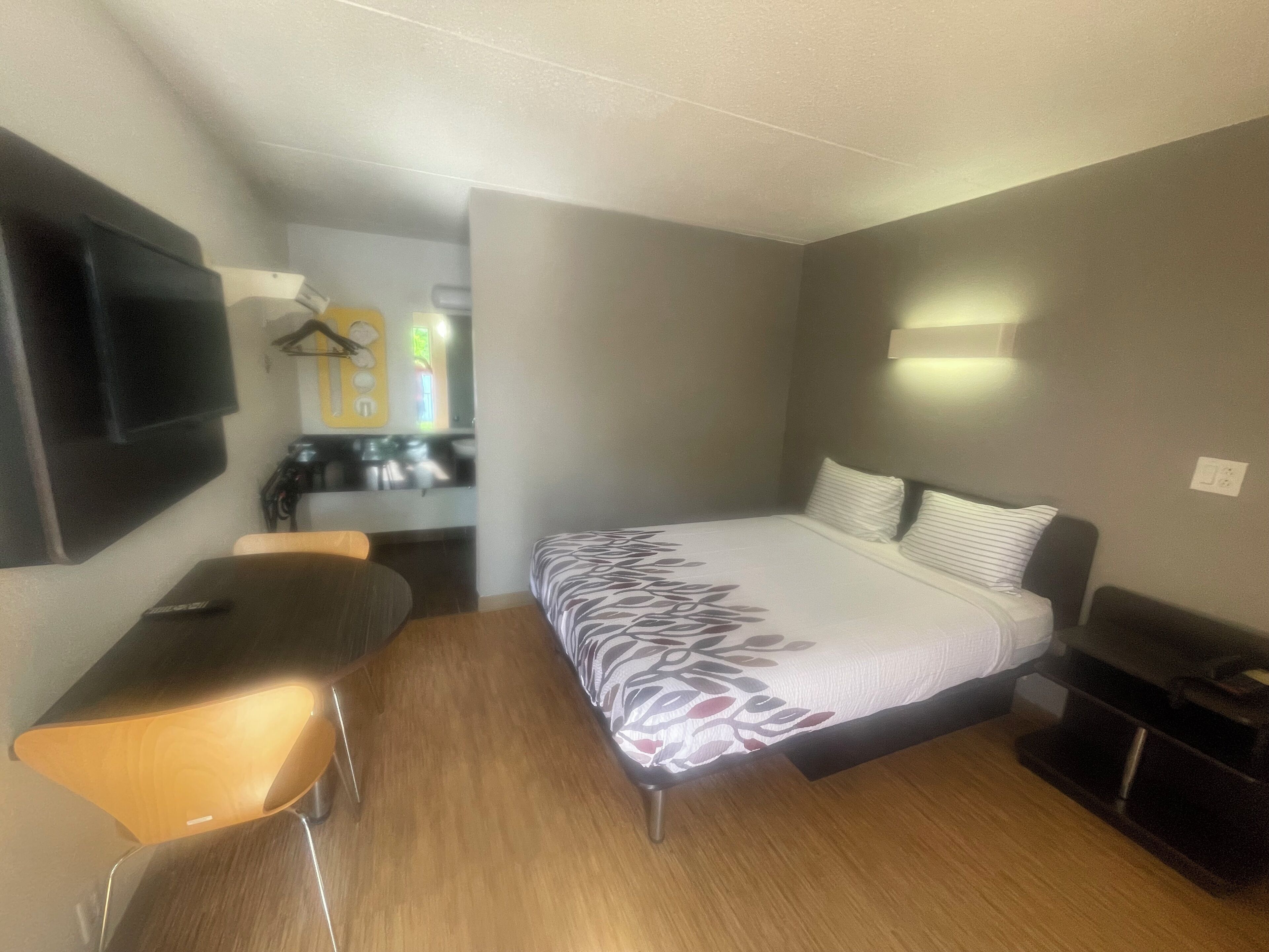 Una habitación de hotel con cama, escritorio, silla, televisor montado en la pared y una pequeña zona de kitchenette.