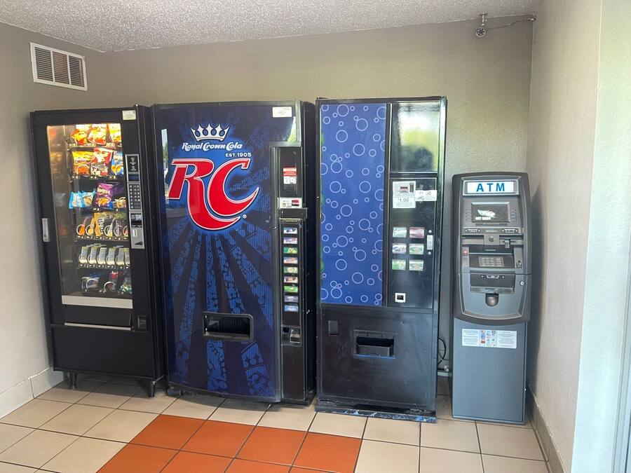 Une rangée de distributeurs automatiques, dont un qui vend du Royal Crown Cola, un autre avec un motif bleu et un distributeur de billets.