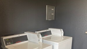 Een wasruimte met twee witte voorladers en een metalen berging aan de muur.