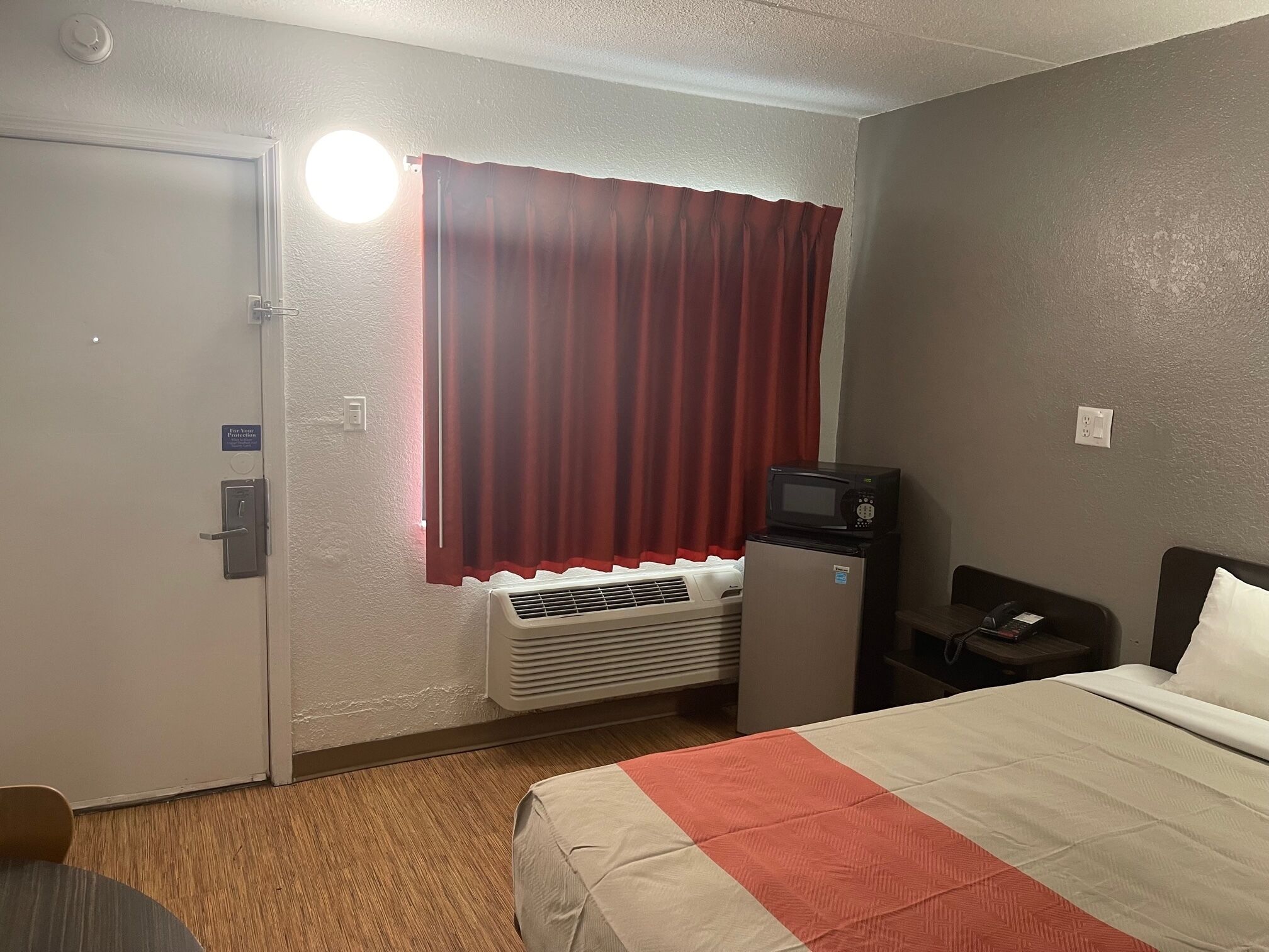 A hotel room with a bed, a desk, a microwave, and a heater.