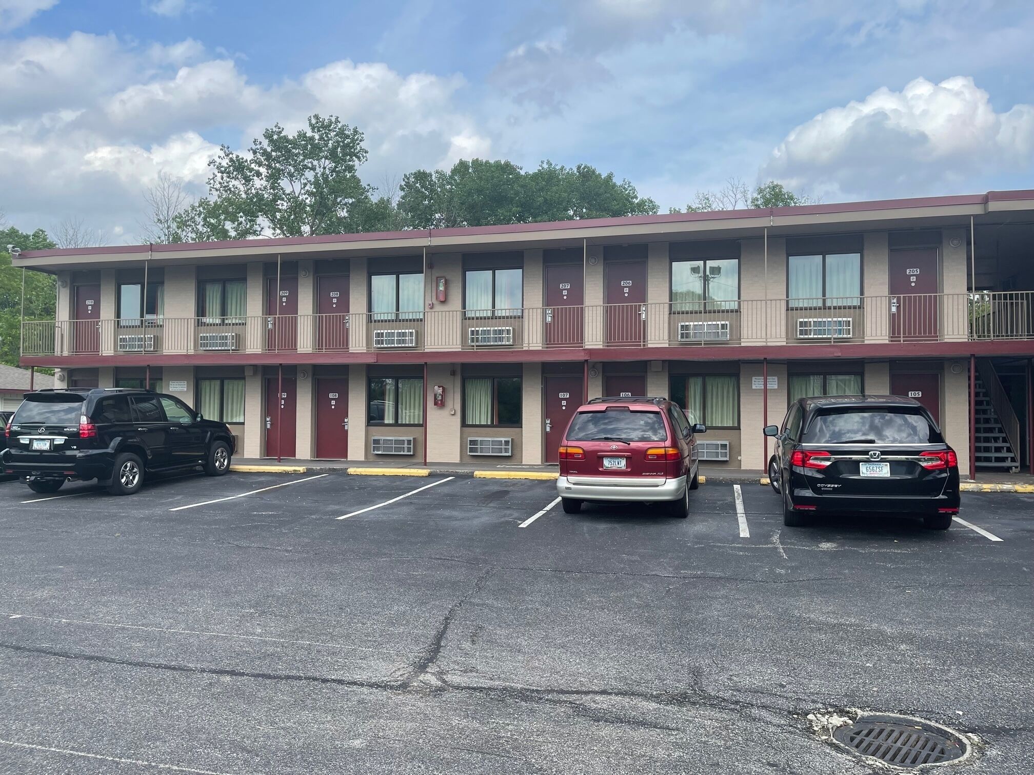 Un motel avec trois places de stationnement, une voiture rouge et noire garée au centre, et une voiture noire sur la gauche.