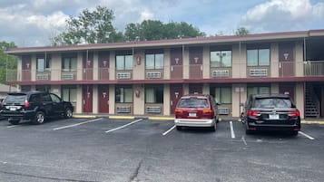 Un motel avec trois places de stationnement, une voiture rouge et noire garée au centre, et une voiture noire sur la gauche.