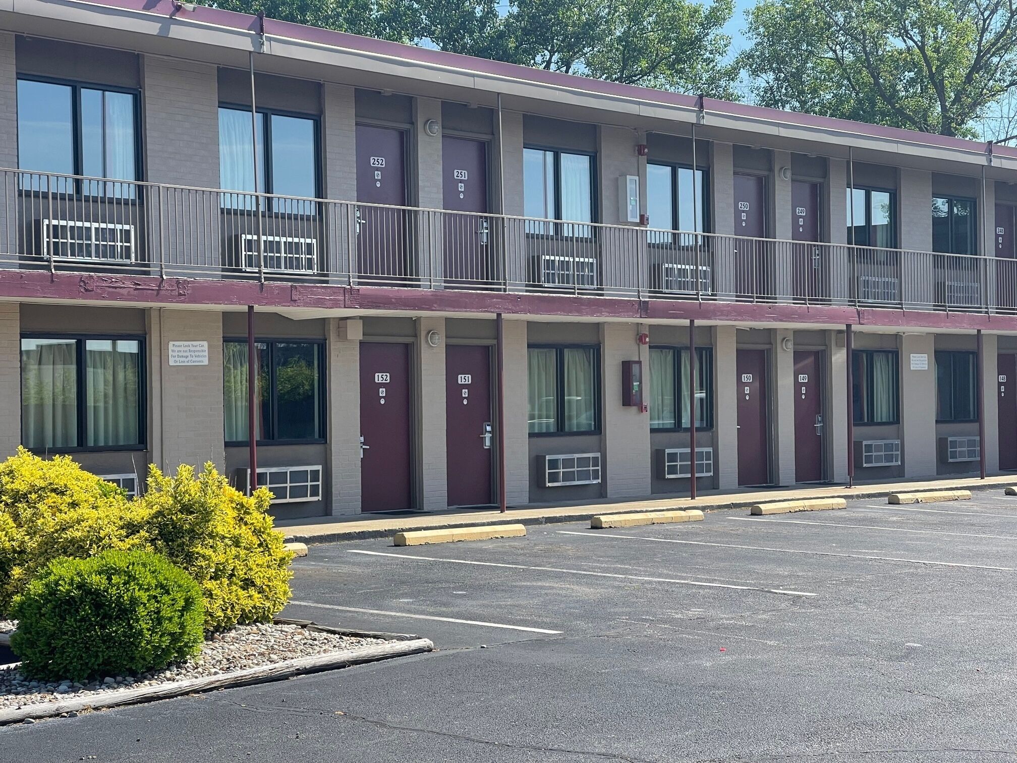 Un motel à plusieurs étages, avec des chambres numérotées, un parking et un petit jardin.