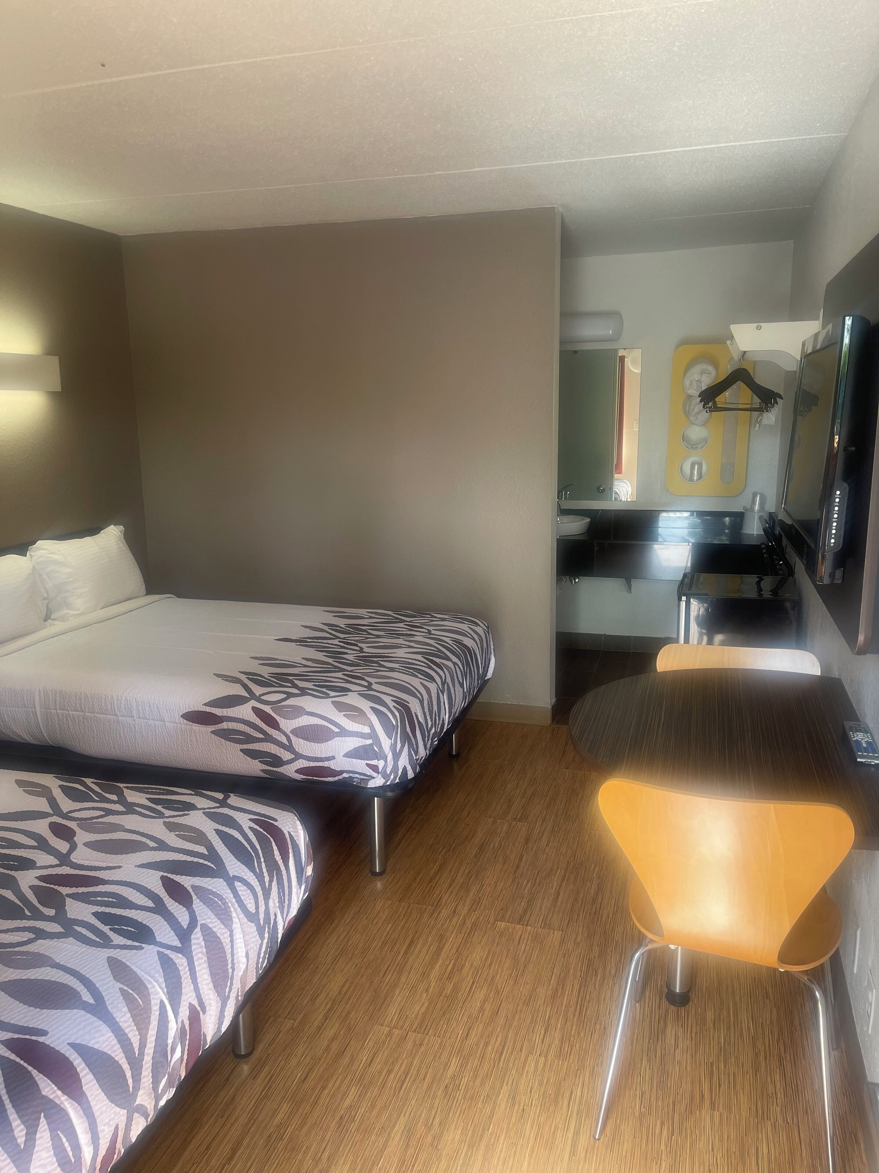 Habitación de hotel con dos camas, un escritorio pequeño, una silla, un espejo y un televisor.