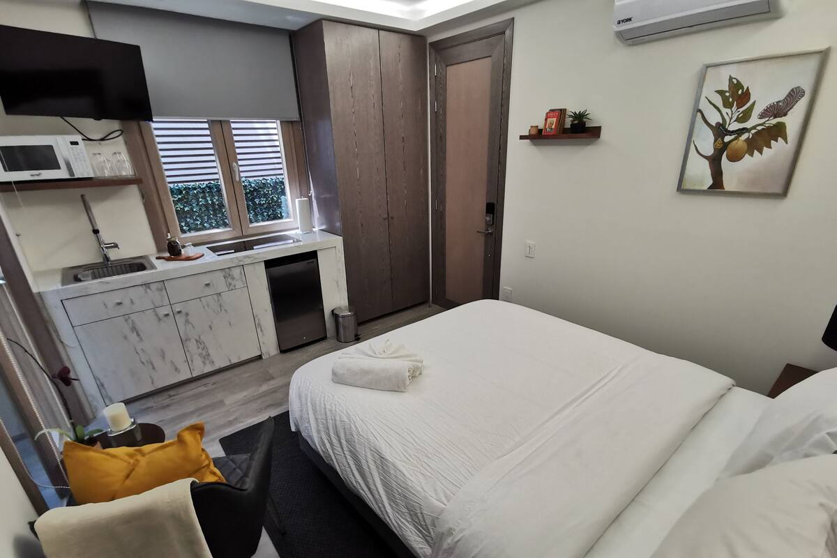 A modern hotel room with a bed, a desk with a chair, a microwave, and a sink.