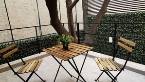Ein Holztisch mit einem Blumentopf, zwei Holzstühle und ein Metallgeländer in einem Innenhof.