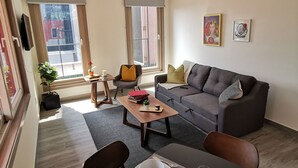 Ein modernes Wohnzimmer mit grauem Sofa, einem Esstisch gedeckt mit Tellern und Besteck, einem kleinen Couchtisch und einem Blumentopf.