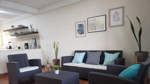 A modern living room with a dark-colored sofa set, a coffee table, and a small side table. There are potted plants and framed artwork on the walls.