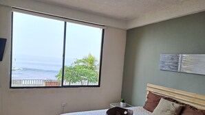 A bedroom with a large window, a bed with a storage box, and a view of the ocean.