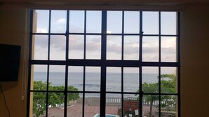 A large window with a view of the sea and a brick pathway leading to a pool.