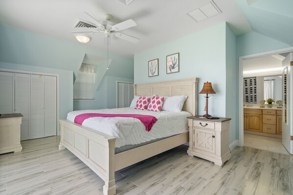 A bedroom with a bed, bedside table, and a ceiling fan. - Beach, Ocean View Pool, King Bed - Walking distance to Restaurants & the Beach! (Nassau)
