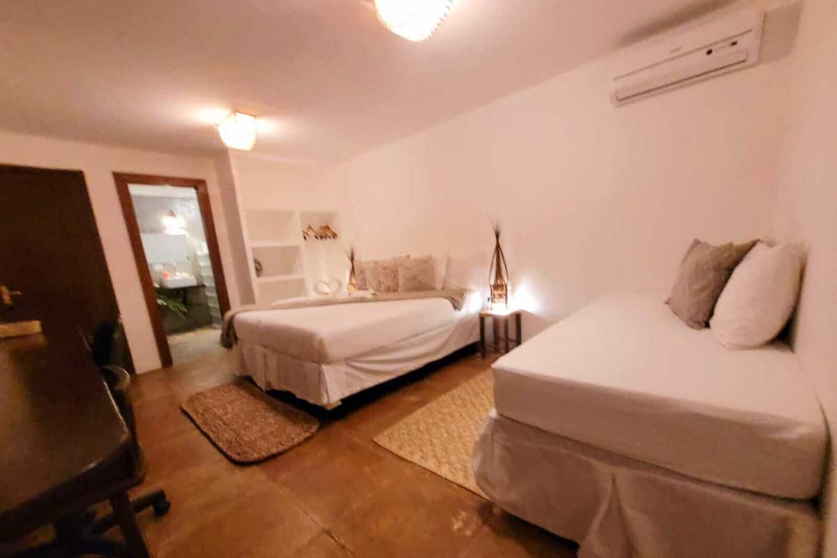 Ein Zimmer mit zwei Einzelbetten, einem Schreibtisch und einem Stuhl. Es gibt einen kleinen Tisch mit einer Lampe und eine Wand-Klimaanlage.