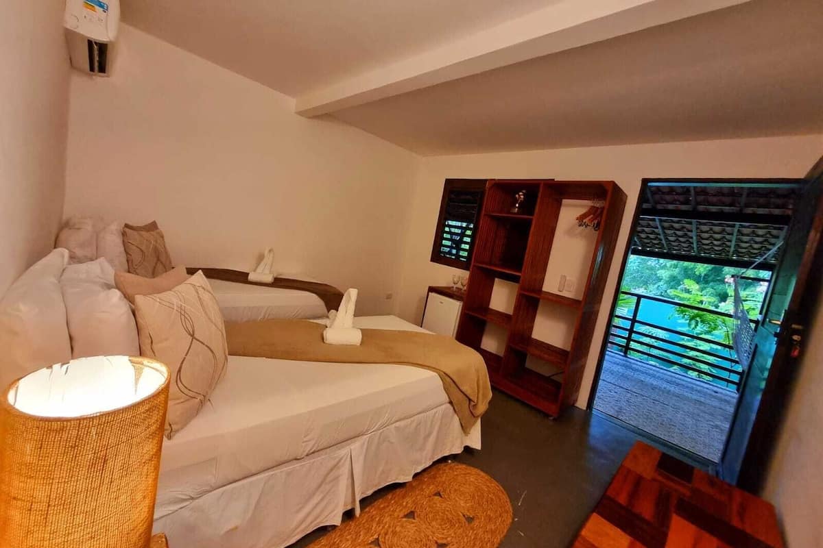 Ein Hotelzimmer mit zwei Betten, einem Nachttisch, einer Lampe, einer kleinen Ablagefläche und Blick ins Freie.