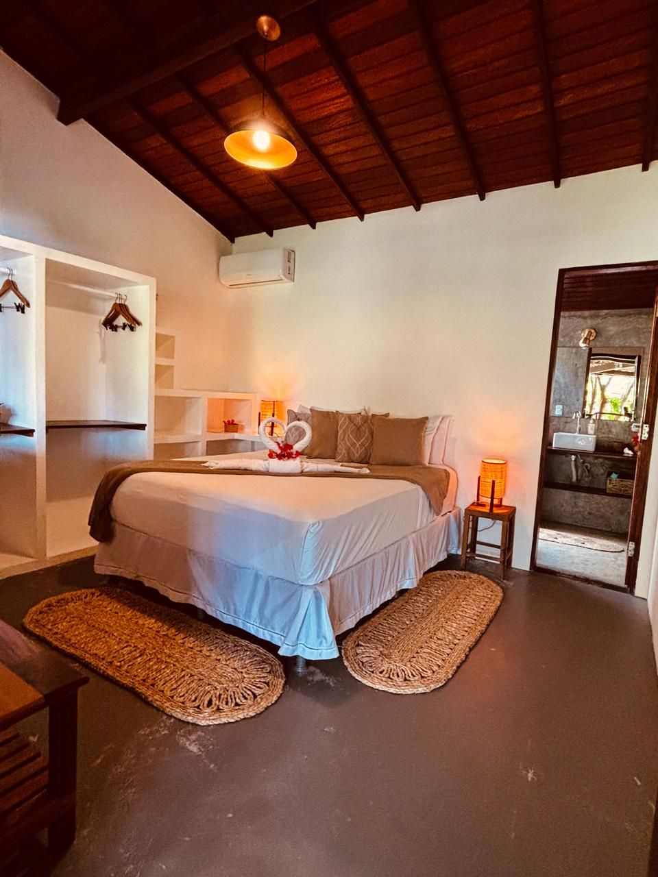 A bedroom with a bed, bedside table, hanging clothes rack, and a small stool.
