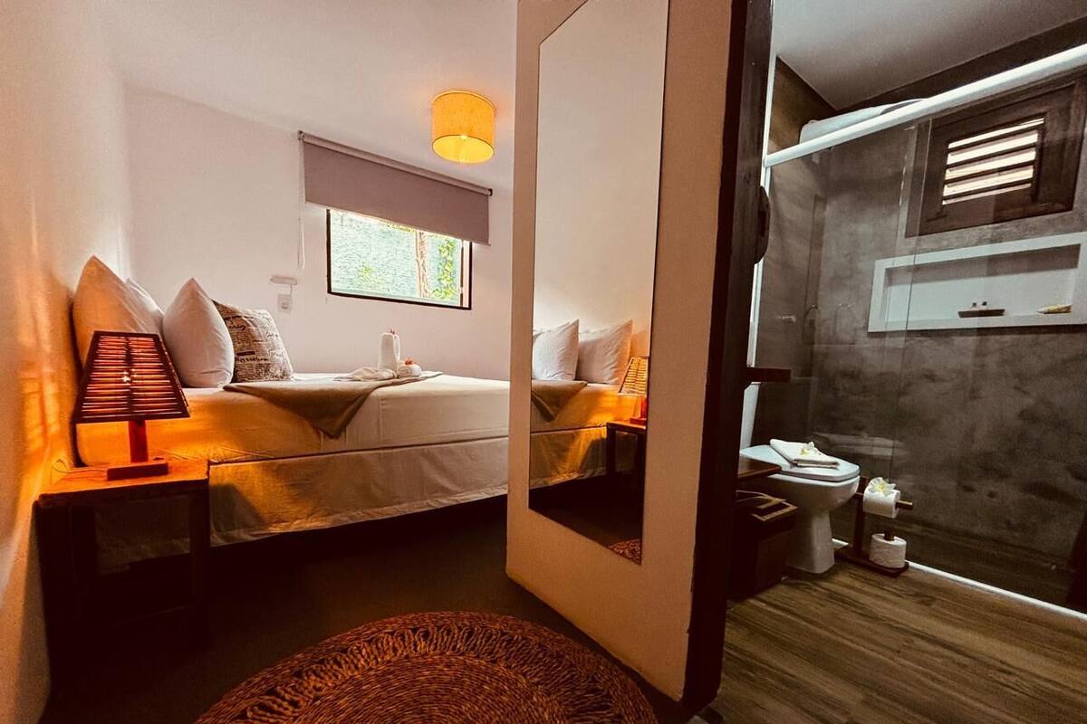 Ein Schlafzimmer mit zwei Betten, einem Nachttisch mit Lampe, einem Spiegel und Blick ins Badezimmer.