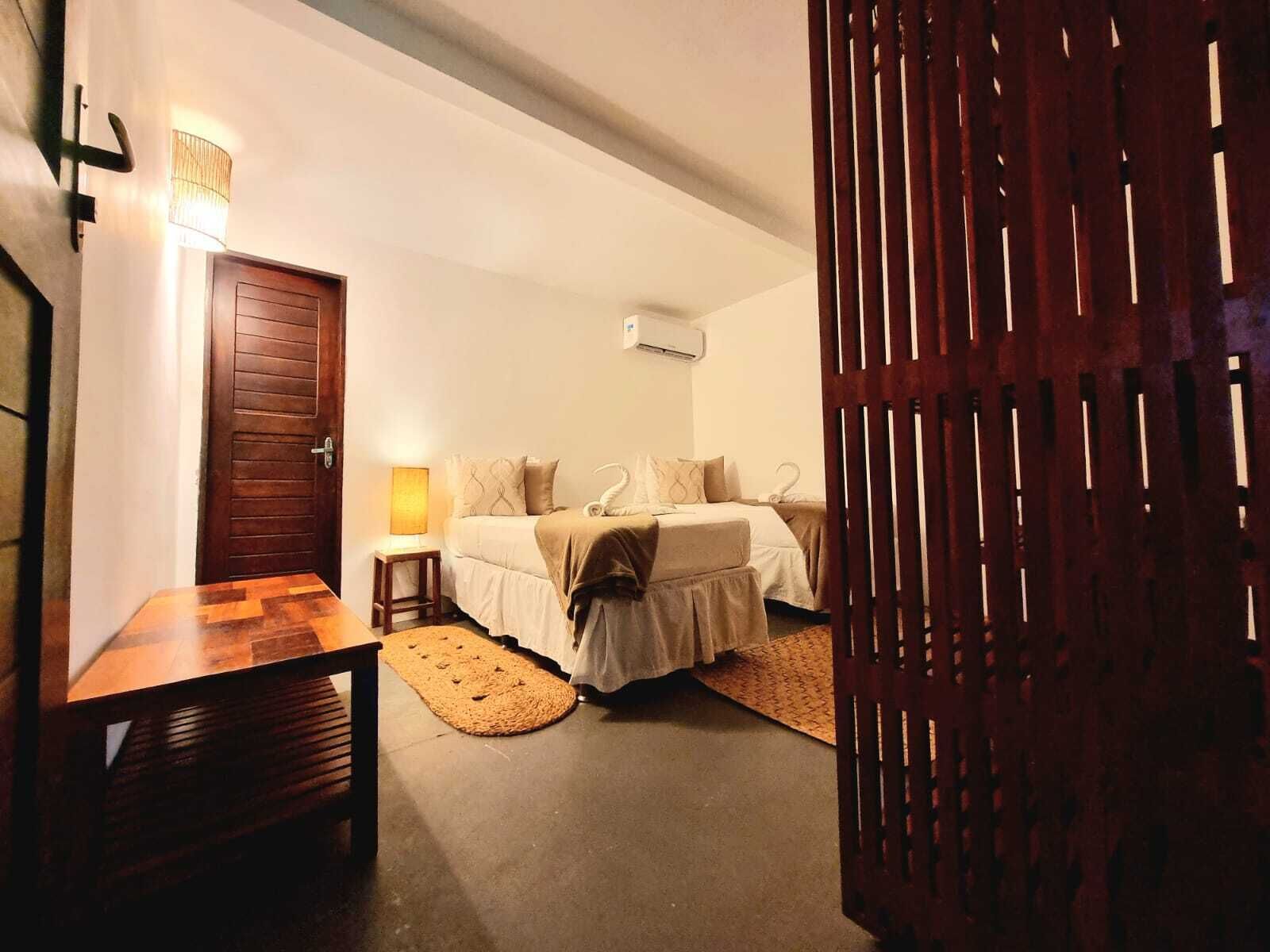 A bedroom with two beds, a wooden door, a small table, and a lamp.
