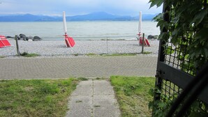 A paved pathway leading to a rocky shore with red barriers and a view of a calm body of water and distant mountains.