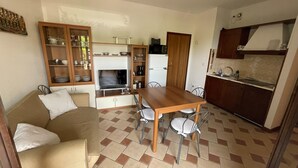 A compact living space with a kitchenette, a dining table with chairs, a sofa, and a cabinet with dishes.