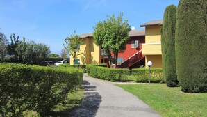 A pathway leading to a building with a red and yellow facade, surrounded by well-maintained hedges and trees.