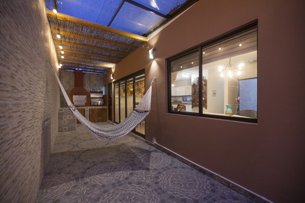A hallway with a hammock, a brick wall, and a glass door leading to a room.