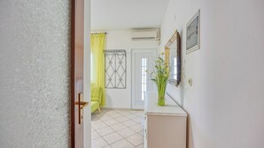 A hallway with a door leading to a room, a yellow chair, a white vase with flowers, and a framed mirror on the wall. - Apartment Mirjana for two people, quiet location, barbecue, pets welcome (Fažana)