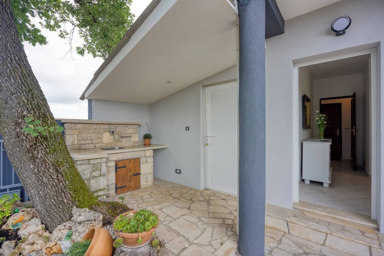 A stone-floored outdoor area with a built-in sink and a door leading to an interior space.