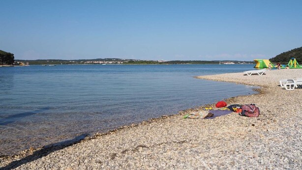 A pebbled beach with clear water, a few tents, and a distant shoreline with buildings. - Apartment Mirjana for two people, quiet location, barbecue, pets welcome (Fažana)