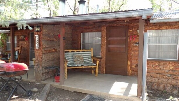 A rustic cabin with a wooden exterior, a bench outside, and a red grill.