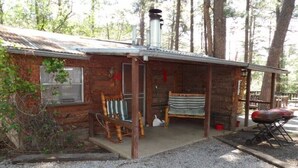 A rustic cabin with a chimney, a porch with a rocking chair, and a barbecue grill.