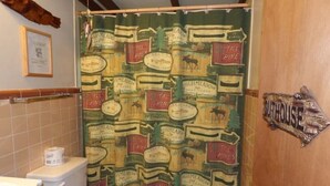 A bathroom with a shower curtain featuring a vintage design, a toilet, a sink, and a wooden door with a sign.